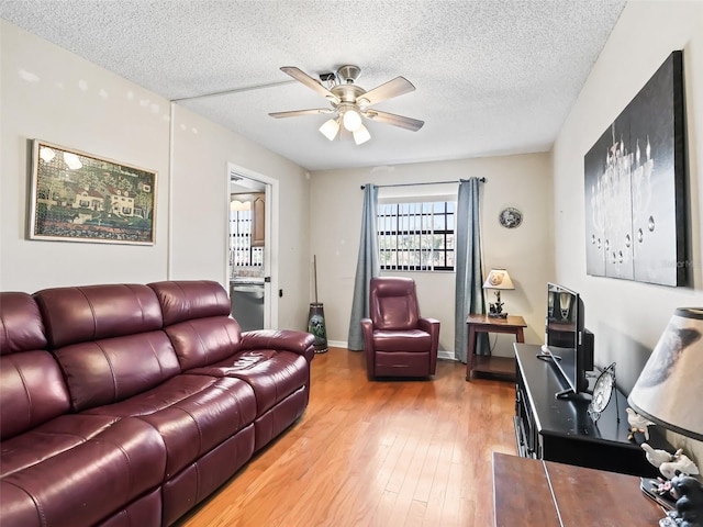 living room with baseboards, ceiling fan, a textured ceiling, and light wood-style flooring