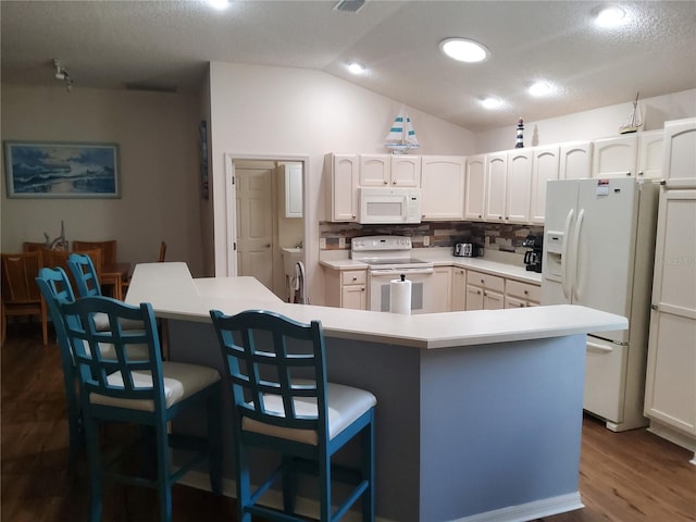 kitchen featuring a kitchen breakfast bar, white appliances, lofted ceiling, and dark wood finished floors
