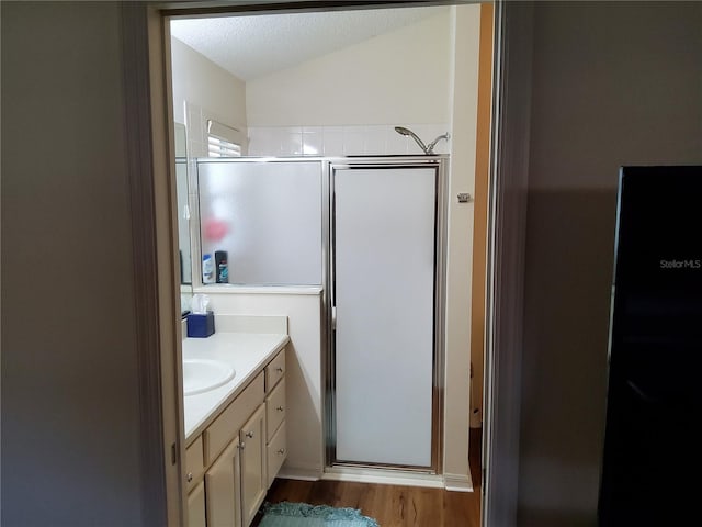 bathroom with wood finished floors, a shower stall, lofted ceiling, and vanity