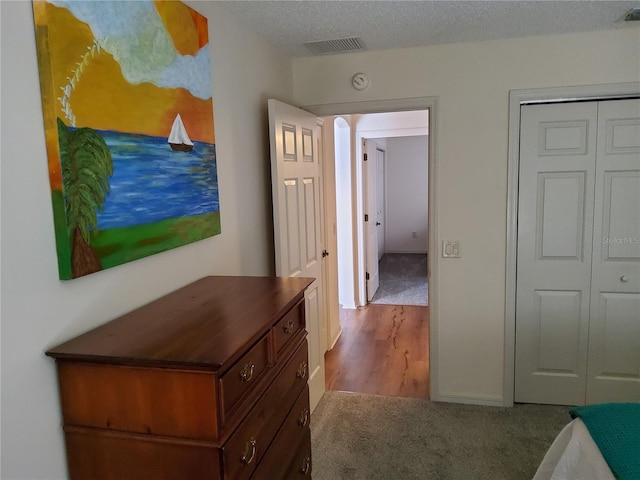 hallway with a textured ceiling, visible vents, wood finished floors, and carpet floors