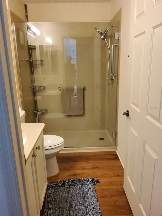 bathroom featuring toilet, vanity, wood finished floors, and a stall shower