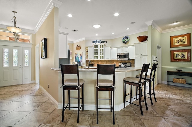 kitchen featuring a peninsula, a kitchen bar, decorative backsplash, appliances with stainless steel finishes, and ornamental molding
