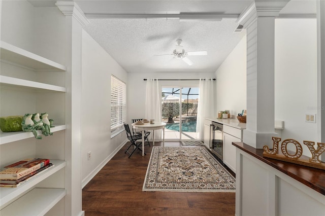 dining space featuring dark wood-style floors, a textured ceiling, ornate columns, a ceiling fan, and beverage cooler