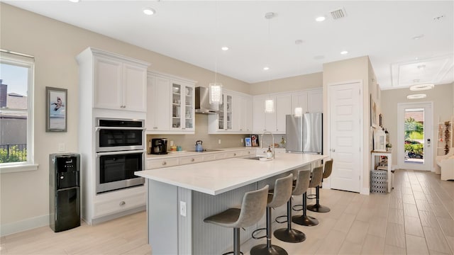 26516 Savage Cir, Howey In The Hills, FL 34737 - kitchen with wall chimney range hood, stainless steel appliances, a sink, white cabinets, and a breakfast bar