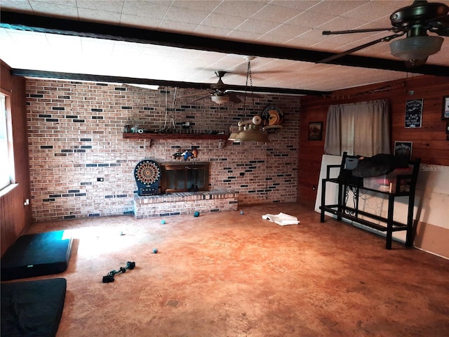 living room with wood walls, a ceiling fan, beam ceiling, a brick fireplace, and brick wall