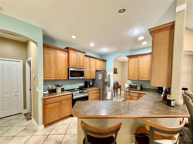 30554 Quince Ave, Eustis, FL 32736 - kitchen featuring stainless steel appliances, arched walkways, a peninsula, a breakfast bar area, and light tile patterned floors