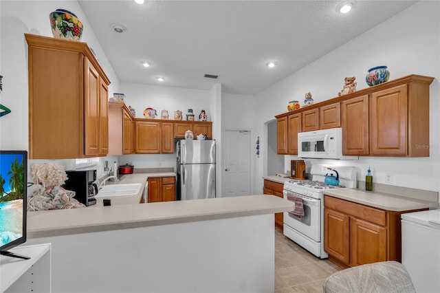 kitchen featuring a peninsula, a sink, white appliances, brown cabinets, and light countertops