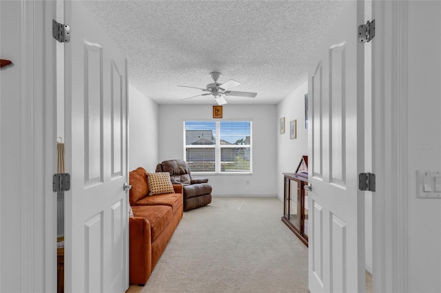 living area featuring a textured ceiling, light carpet, baseboards, and ceiling fan
