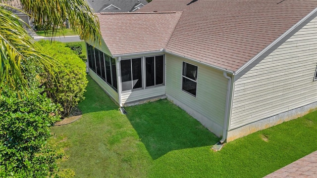 exterior space with a yard, a sunroom, and roof with shingles
