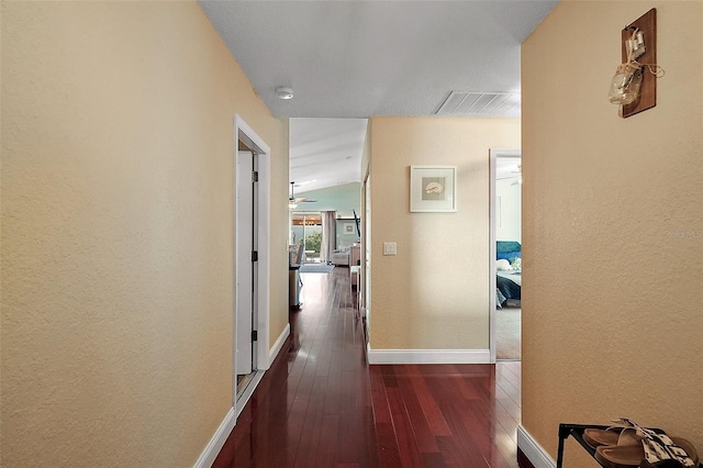 hall with dark wood-type flooring, visible vents, a textured wall, and baseboards