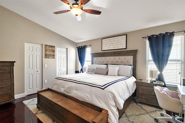 bedroom featuring two closets, ceiling fan, baseboards, vaulted ceiling, and wood finished floors