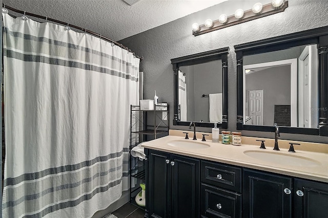 bathroom with double vanity, a sink, a textured wall, and tile patterned floors