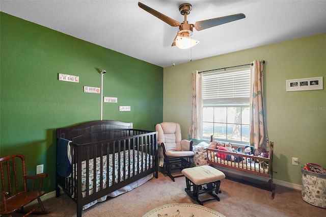 bedroom with a crib, ceiling fan, carpet floors, and baseboards