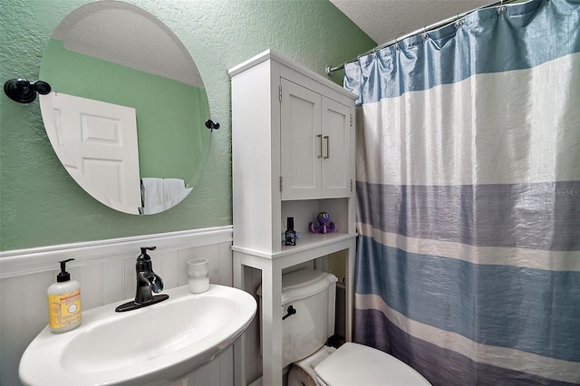 bathroom with a sink, toilet, a wainscoted wall, a textured wall, and a shower with shower curtain