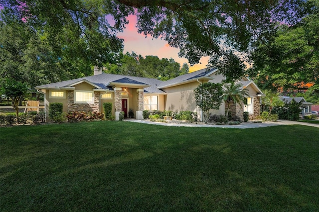 view of front of house with a lawn, a chimney, stucco siding, and stone siding