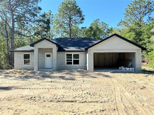 property under construction with dirt driveway, an attached garage, and a shingled roof
