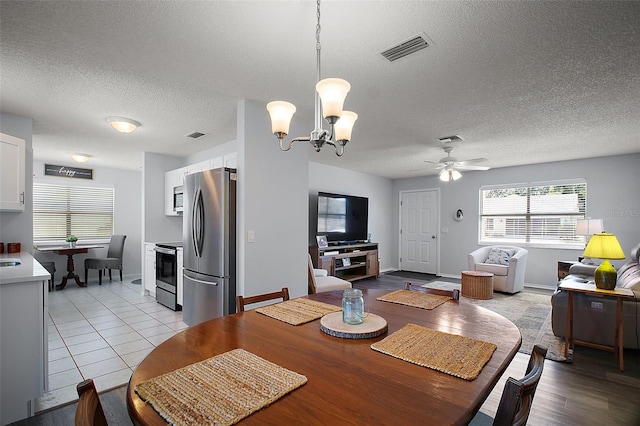 dining room with ceiling fan with notable chandelier, visible vents, a textured ceiling, and a healthy amount of sunlight