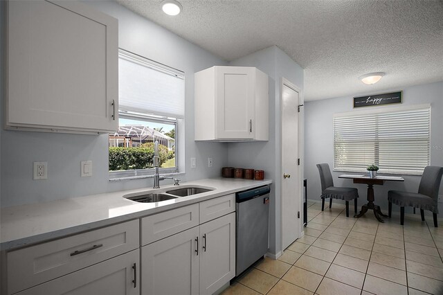 kitchen with stainless steel dishwasher, light countertops, a sink, and a textured ceiling