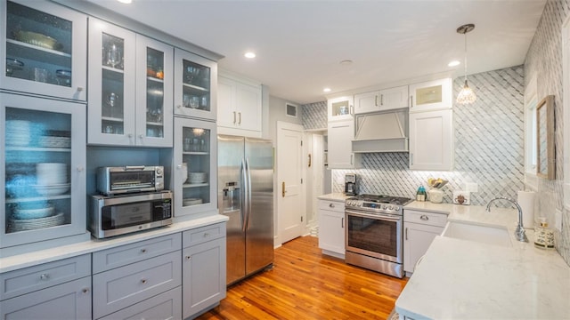 908 N Tremain St, Mount Dora, FL 32757 - kitchen with exhaust hood, decorative light fixtures, a sink, light wood finished floors, and stainless steel appliances