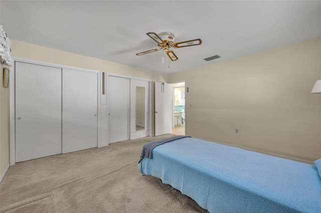 bedroom with two closets, light carpet, a ceiling fan, and visible vents