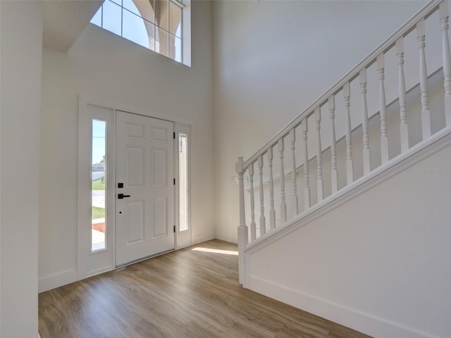 entrance foyer with stairway, baseboards, a towering ceiling, and wood finished floors
