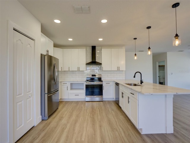kitchen with visible vents, a sink, light wood-style floors, wall chimney exhaust hood, and appliances with stainless steel finishes