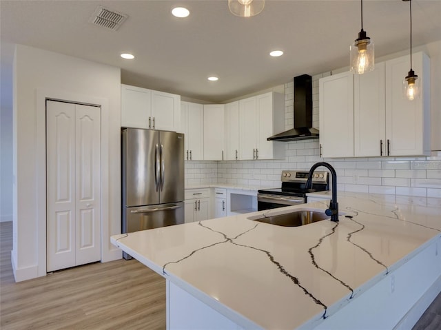 kitchen with wall chimney range hood, a sink, stainless steel appliances, a peninsula, and visible vents