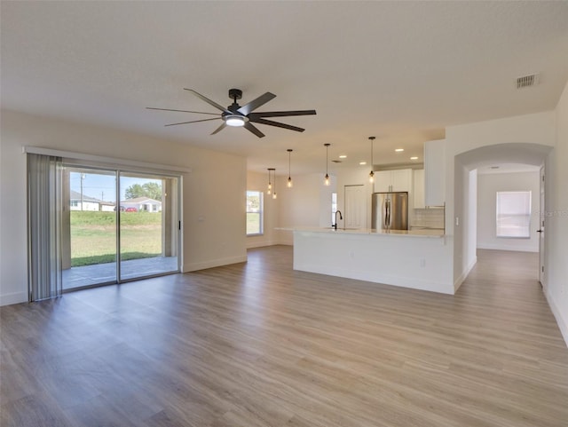 unfurnished living room with visible vents, a sink, arched walkways, baseboards, and ceiling fan