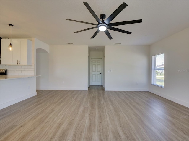 unfurnished living room featuring light wood finished floors, visible vents, arched walkways, baseboards, and ceiling fan