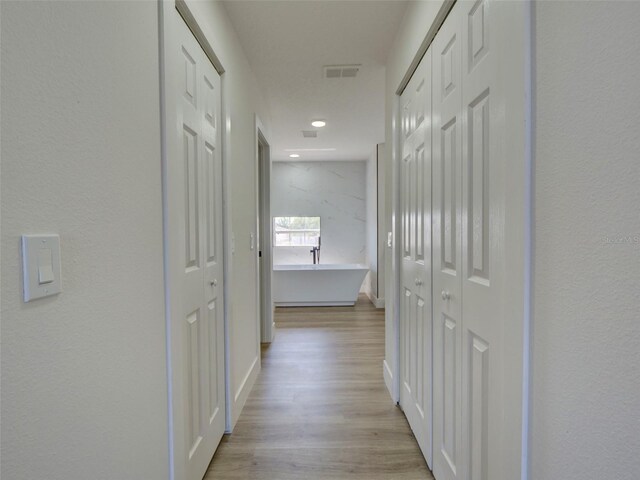 hallway with light wood-type flooring, visible vents, and baseboards
