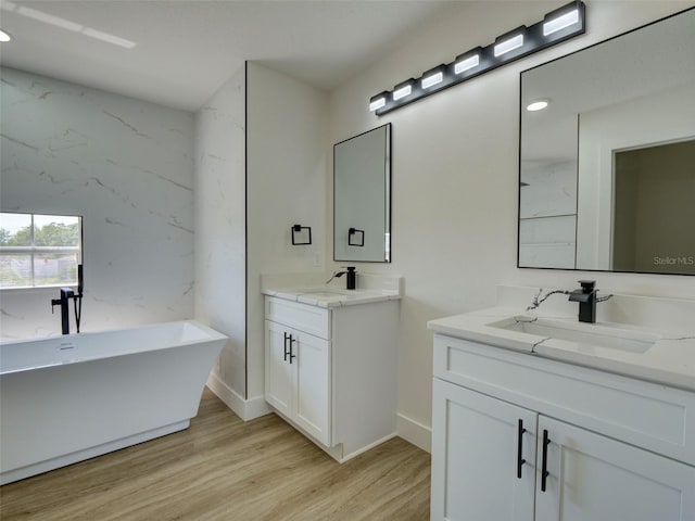 bathroom with a freestanding bath, two vanities, wood finished floors, and a sink