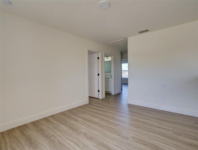 empty room featuring attic access, visible vents, light wood finished floors, and baseboards