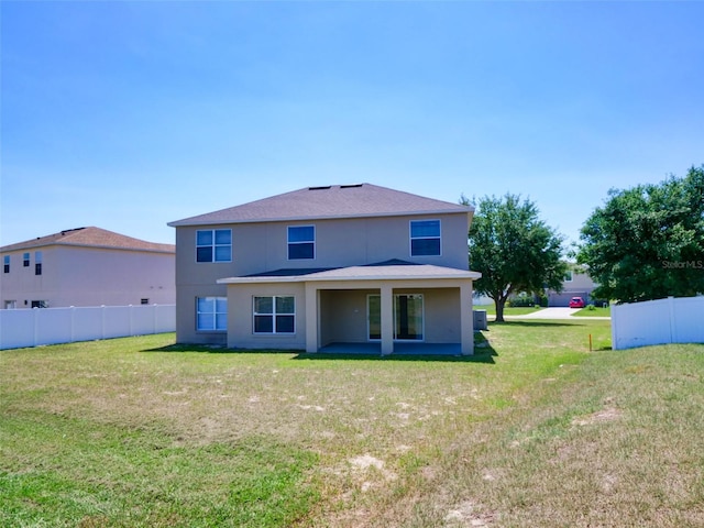rear view of house with stucco siding, fence, and a yard