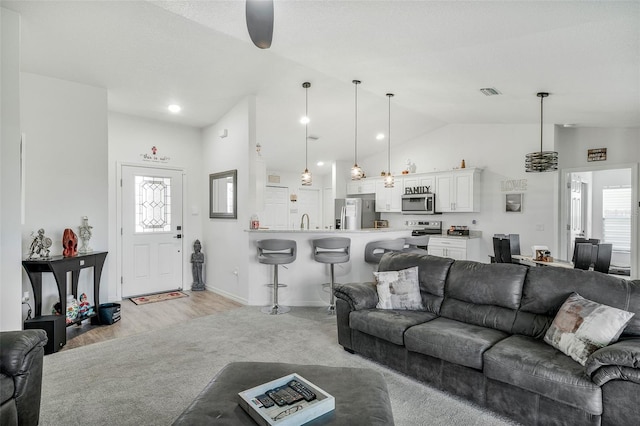 living area featuring light wood finished floors, vaulted ceiling, baseboards, visible vents, and a ceiling fan