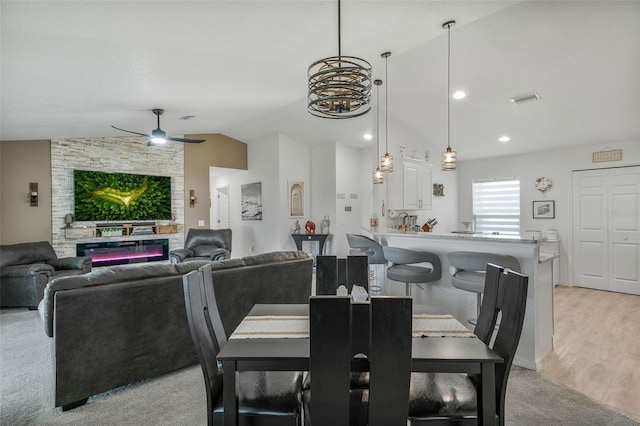 dining space with a ceiling fan, a stone fireplace, light wood-style flooring, lofted ceiling, and visible vents
