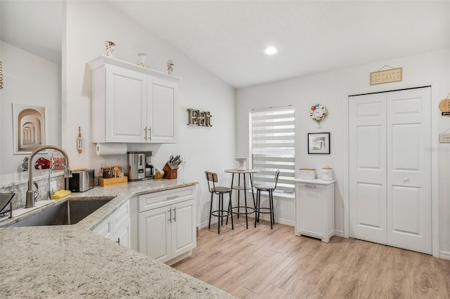kitchen featuring a sink, light wood-type flooring, lofted ceiling, white cabinetry, and light stone countertops