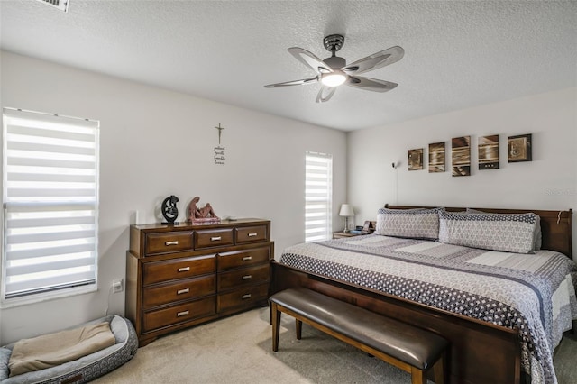 bedroom with a textured ceiling, light colored carpet, and ceiling fan