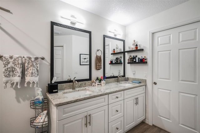 bathroom featuring double vanity, a textured ceiling, wood finished floors, and a sink
