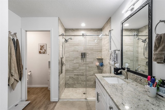 bathroom with a shower stall, wood finished floors, vanity, baseboards, and a textured ceiling