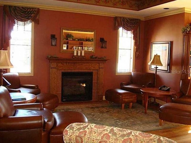 living area with crown molding, wood finished floors, and a fireplace with raised hearth