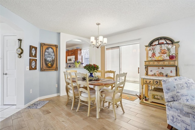 732 Ramirez Ave, The Villages, FL 32159 - dining room featuring light wood-type flooring, arched walkways, a textured ceiling, and a notable chandelier
