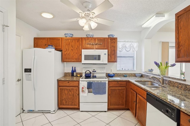 732 Ramirez Ave, The Villages, FL 32159 - kitchen featuring brown cabinetry, white appliances, arched walkways, a sink, and stone counters