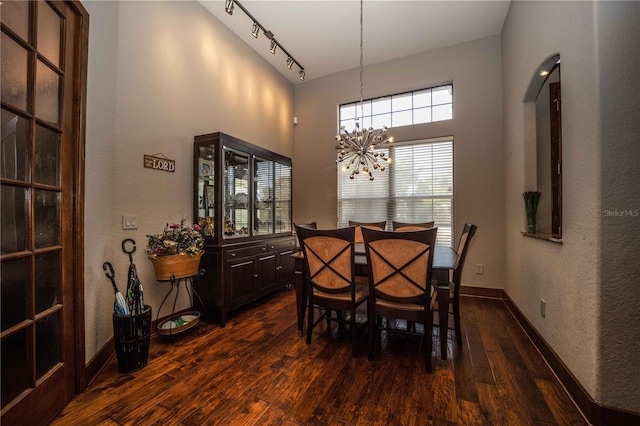 dining space with a chandelier, a textured wall, a towering ceiling, dark wood finished floors, and baseboards