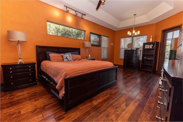 bedroom featuring an inviting chandelier, dark wood-style floors, and a raised ceiling