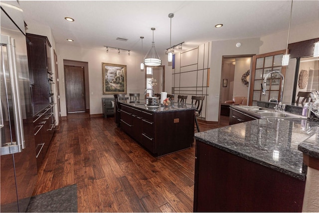 kitchen featuring a sink, dark wood-type flooring, pendant lighting, a center island with sink, and dark brown cabinetry
