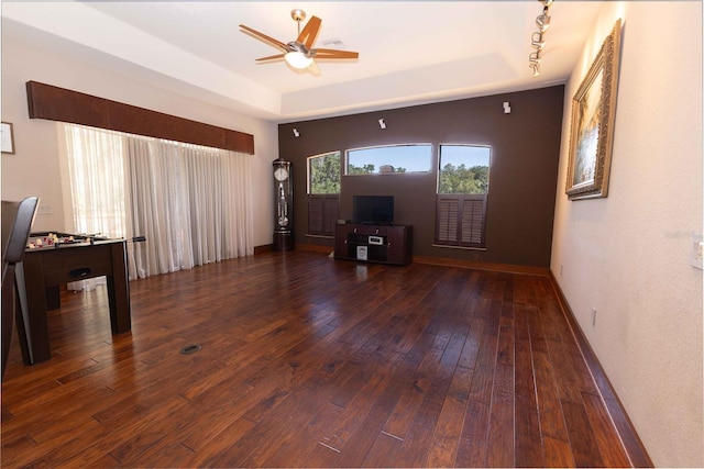 unfurnished living room featuring hardwood / wood-style floors, ceiling fan, baseboards, and a raised ceiling