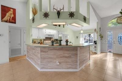 kitchen featuring a peninsula, a high ceiling, light tile patterned flooring, and white cabinets