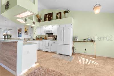 kitchen with a peninsula, white cabinetry, lofted ceiling, white appliances, and hanging light fixtures