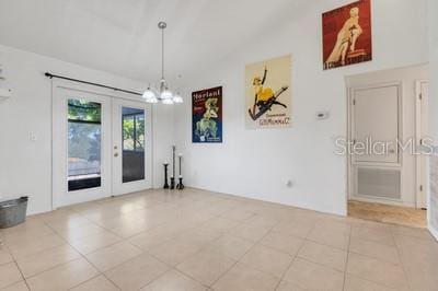 unfurnished dining area with an inviting chandelier, lofted ceiling, french doors, and tile patterned floors