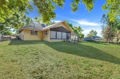 rear view of house featuring fence, a yard, and stucco siding